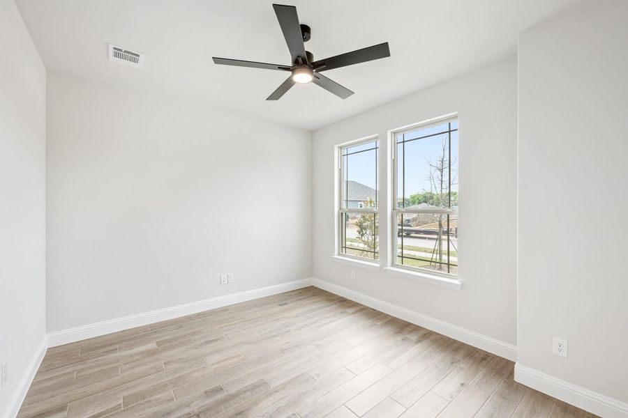 Empty bedroom with light wood floors, black ceiling fan, and two windows
