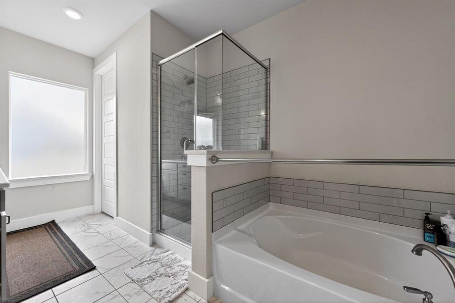 Bathroom featuring a spacious soaking tub, a separate shower with glass enclosure and subway tile, and a frosted window