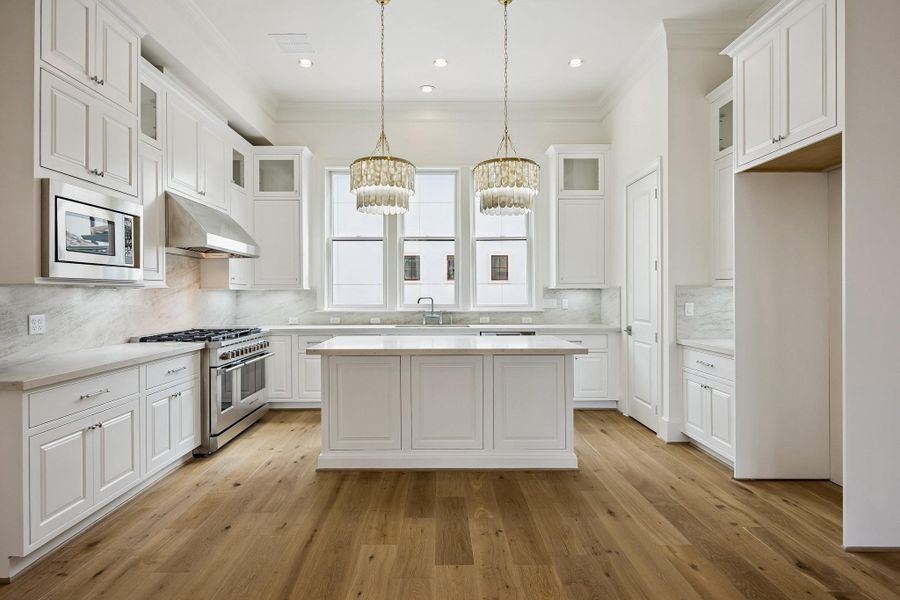 Bright kitchen with large center island, abundant cabinetry and designer pendant lighting.