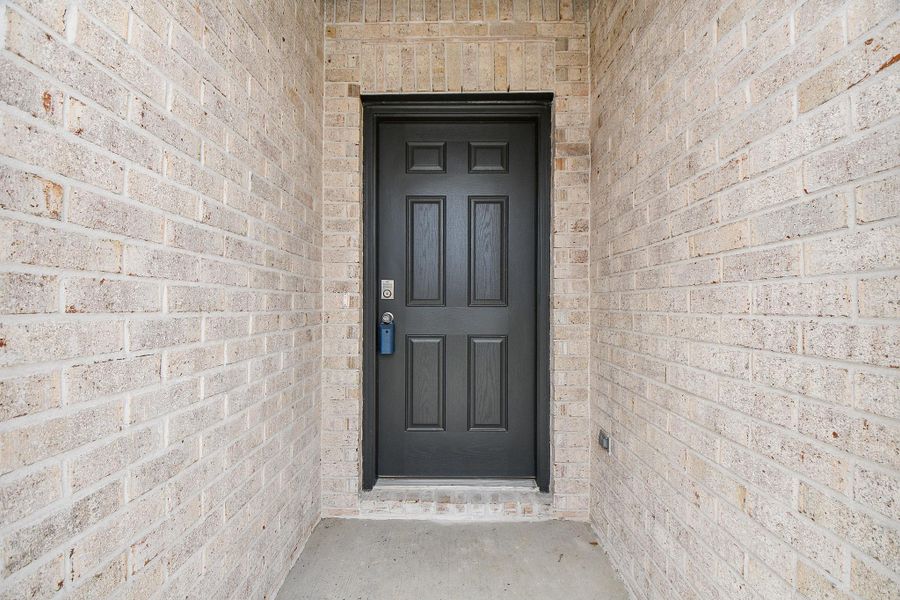 This photo shows a welcoming entryway with a sturdy black front door framed by light brick walls, offering a secure and stylish entrance to the home. This photo shows a welcoming entryway with a sturdy black front door framed by light brick walls, offering a secure and stylish entrance to the home.