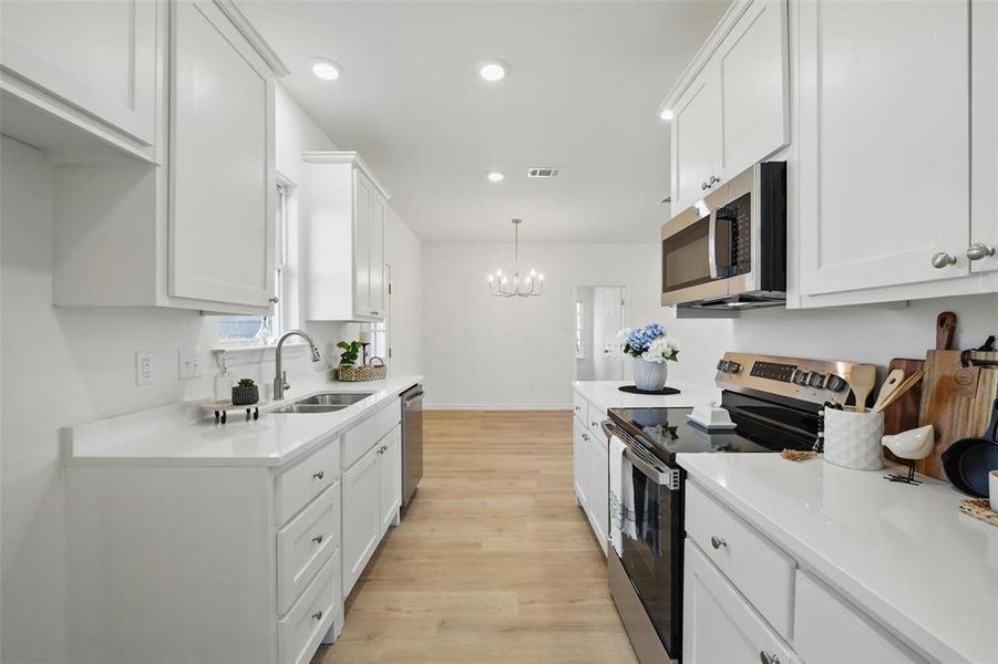 Kitchen featuring stainless steel appliances, a sink, light wood finished floors, white cabinets, and recessed lighting Kitchen featuring stainless steel appliances, a sink, light wood finished floors, white cabinets, and recessed lighting