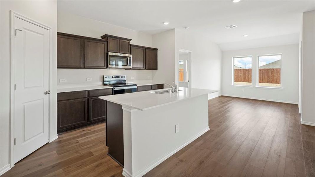 Open-concept kitchen and living area featuring wood-finish flooring, dark wood cabinetry, white countertops, and stainless steel appliances