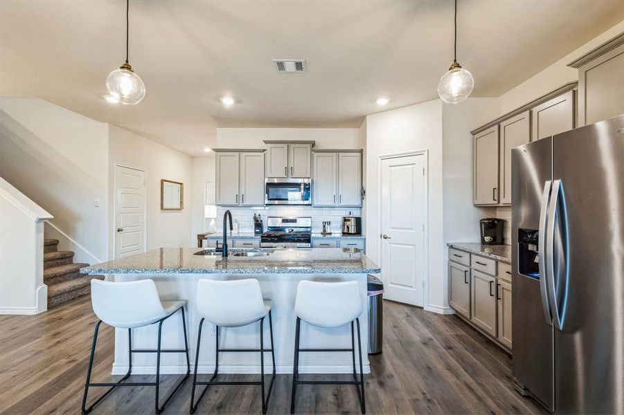 Kitchen with stainless steel appliances, sink, an island with sink, and decorative light fixtures