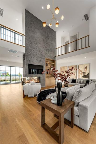 Living area with a high ceiling, light wood finished floors, recessed lighting, a chandelier, and a multi sided fireplace Living area with a high ceiling, light wood finished floors, recessed lighting, a chandelier, and a multi sided fireplace