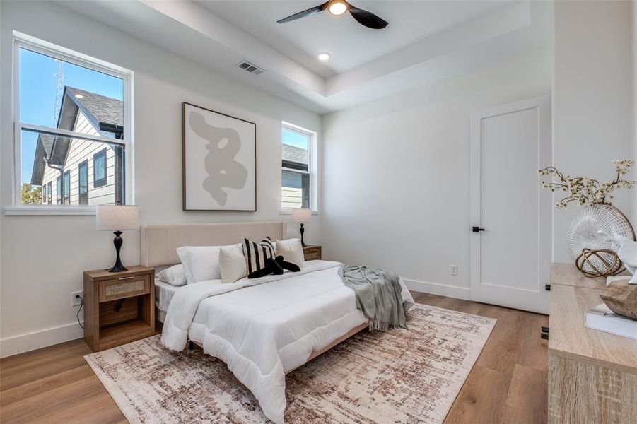 Bedroom with light wood finished floors, a raised ceiling, and a ceiling fan