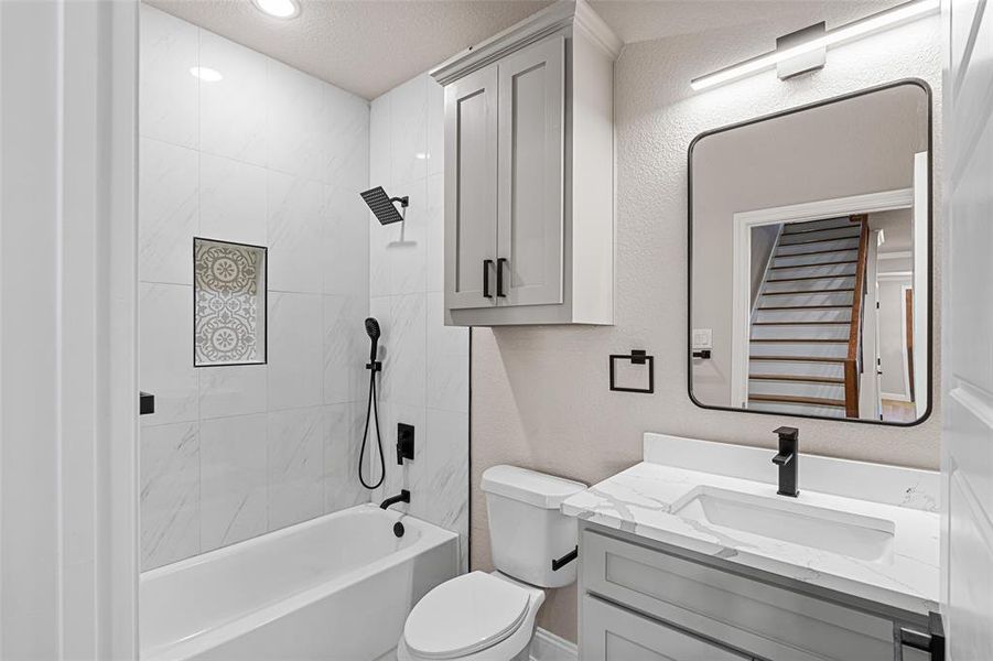 Full bathroom with tiled shower / bath, toilet, a textured ceiling, and vanity