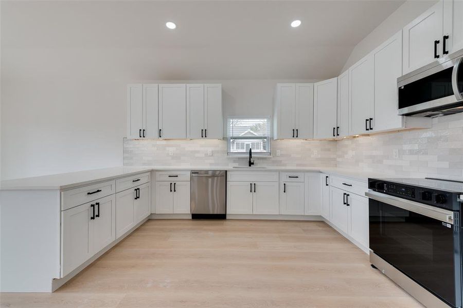 Kitchen featuring appliances with stainless steel finishes, sink, white cabinets, and decorative backsplash