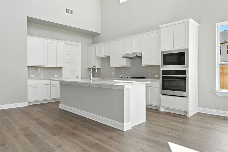Kitchen with backsplash, stainless steel appliances, an island with sink, white cabinets, and a towering ceiling