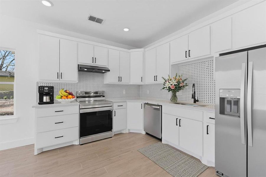 Kitchen with appliances with stainless steel finishes, white cabinetry, light wood finished floors, tasteful backsplash, and under cabinet range hood