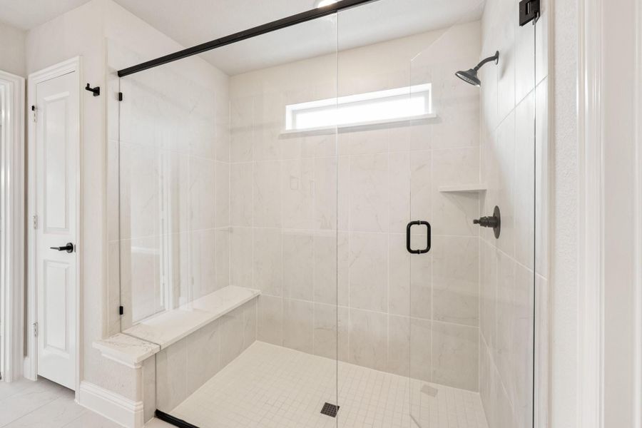 Walk-in shower with white tile walls, glass door, built-in bench, and black hardware fixtures