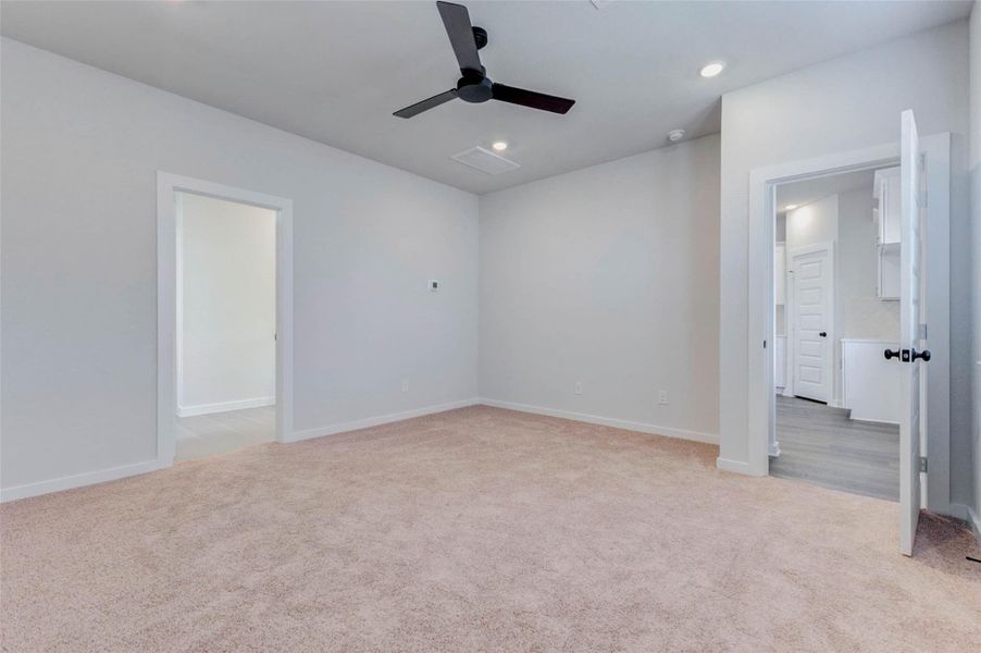 Another view of the spacious primary suite highlights easy access to the ensuite and main living area. Soft carpet underfoot and thoughtful lighting details elevate this serene and versatile retreat designed for comfort and convenience.