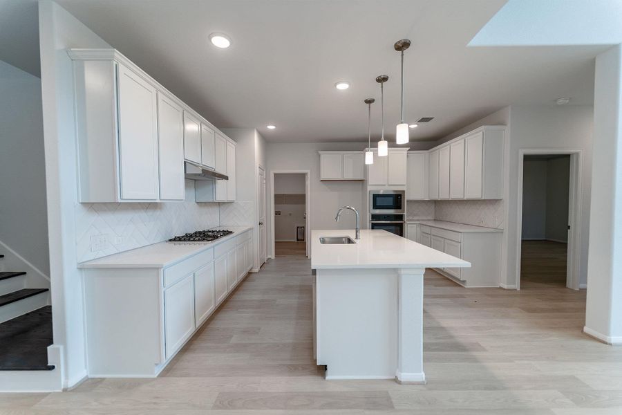 Kitchen featuring white cabinetry, tasteful backsplash, light wood finished floors, a center island with sink, and stainless steel appliances