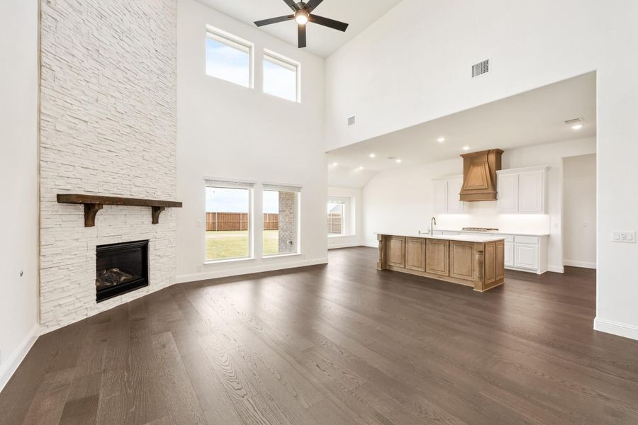 Open living area with two-story stone fireplace, hardwood floors, and open-concept kitchen with wood island beyond