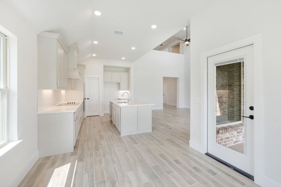 Open kitchen with white cabinets, center island with sink, and light wood-look tile floors