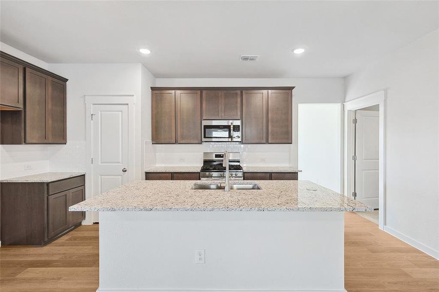 Kitchen featuring appliances with stainless steel finishes, light stone counters, a center island with sink, and light hardwood / wood-style floors