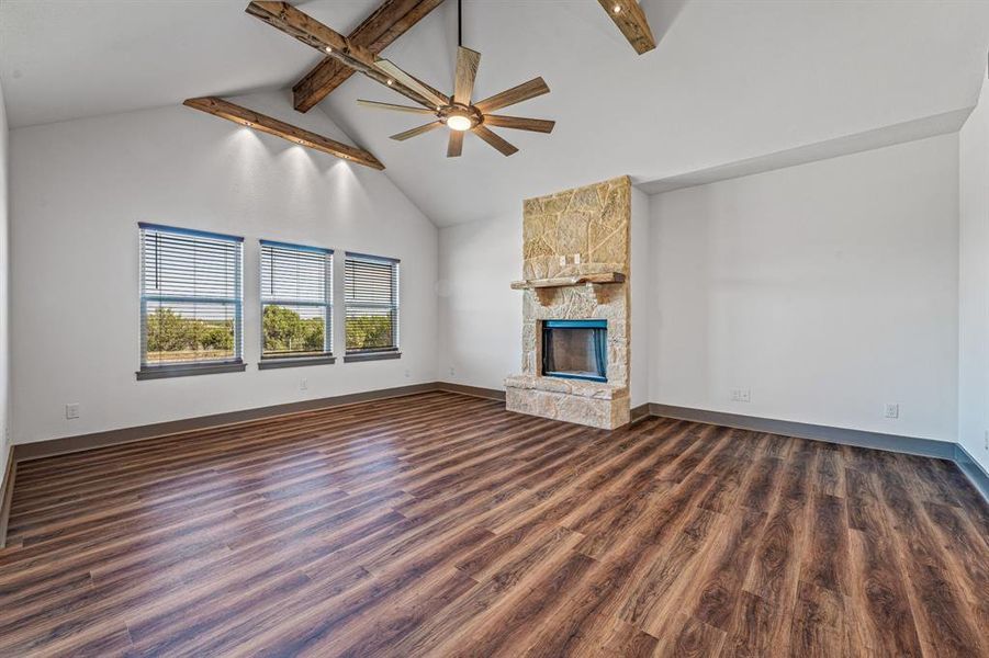 Unfurnished living room with beamed ceiling, high vaulted ceiling, dark wood-style floors, a stone fireplace, and ceiling fan