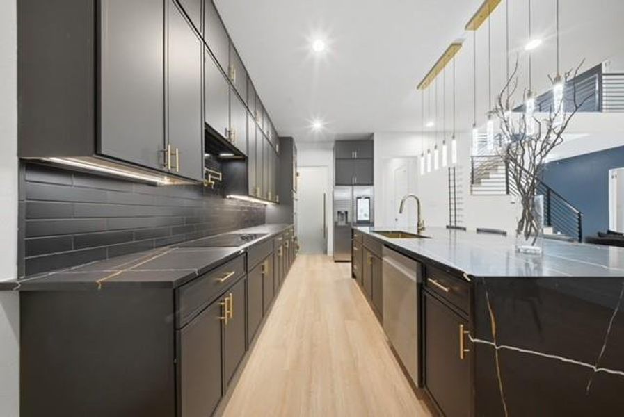 Modern kitchen featuring dark cabinetry with gold-tone hardware, black subway tile backsplash, and light wood-finish flooring