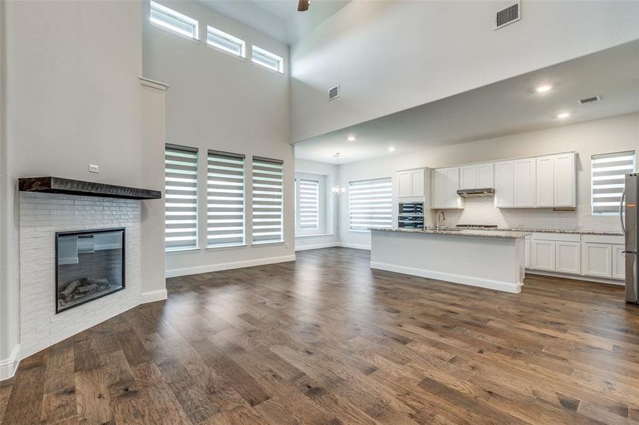 Unfurnished living room featuring a sink, healthy amount of natural light, dark wood finished floors, a brick fireplace, and a high ceiling