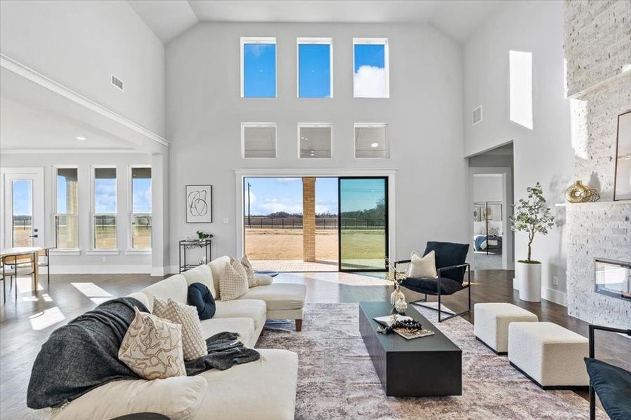 Living room featuring hardwood / wood-style flooring, a stone fireplace, a healthy amount of sunlight, and high vaulted ceiling