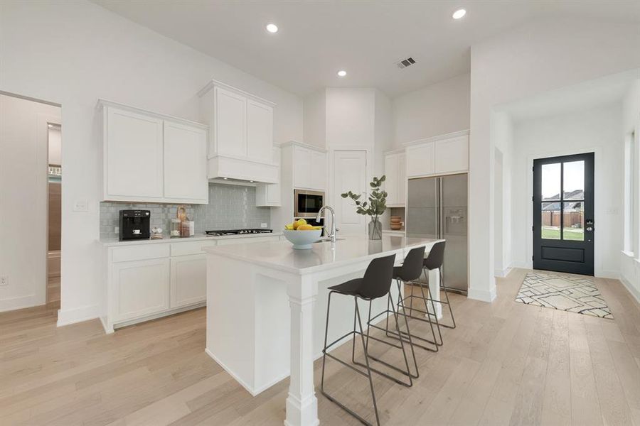Kitchen featuring white cabinets, a breakfast bar area, backsplash, light wood-style flooring, and a center island with sink Kitchen featuring white cabinets, a breakfast bar area, backsplash, light wood-style flooring, and a center island with sink