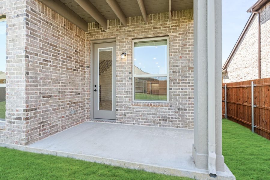 Covered back patio with concrete slab, brick exterior, back door, and fenced yard with green lawn. Covered back patio with concrete slab, brick exterior, back door, and fenced yard with green lawn.