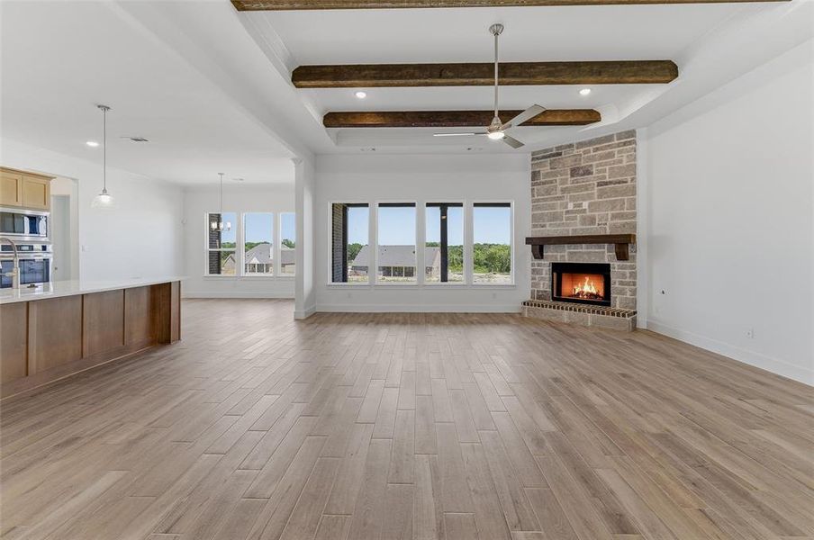 Spacious living area featuring wood-finish flooring, a stone fireplace with a wood mantle, ceiling beams, and a ceiling fan