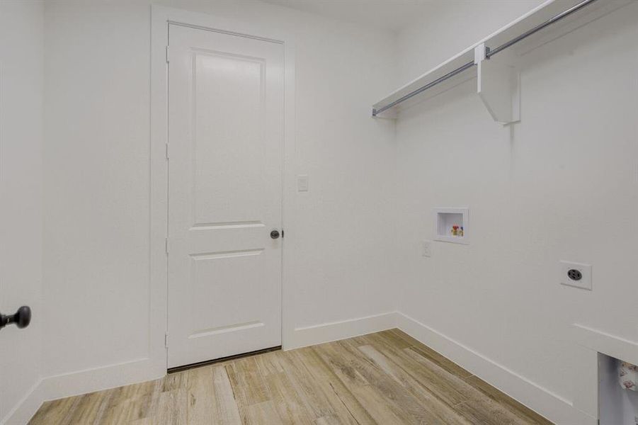 Utility room featuring wood-finish flooring, white walls, and a built-in hanging rod