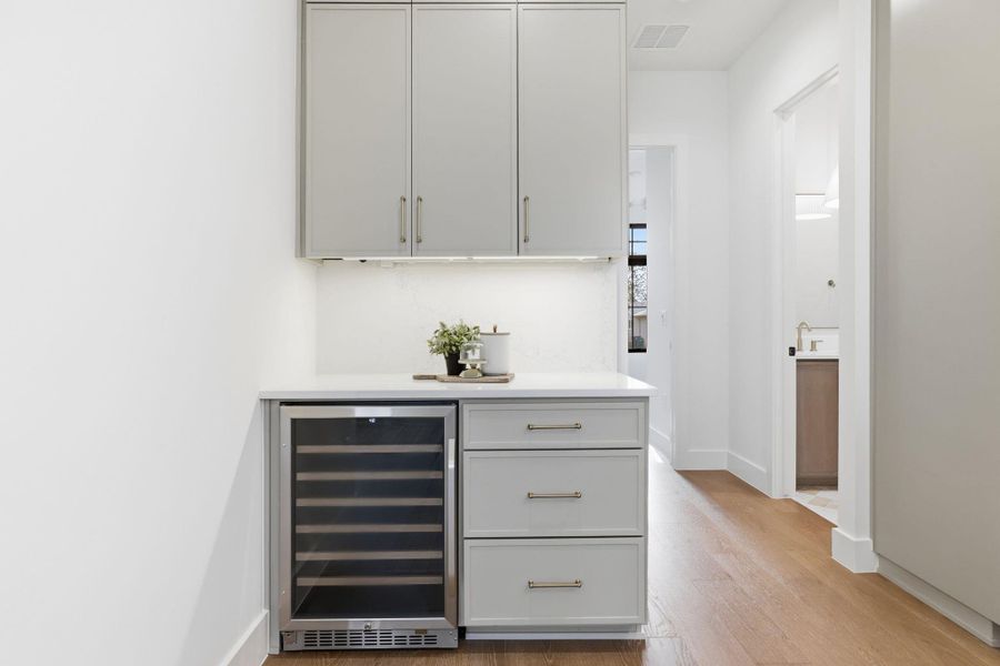 Bar with wine cooler, light wood-style floors, white cabinets, and light stone countertops