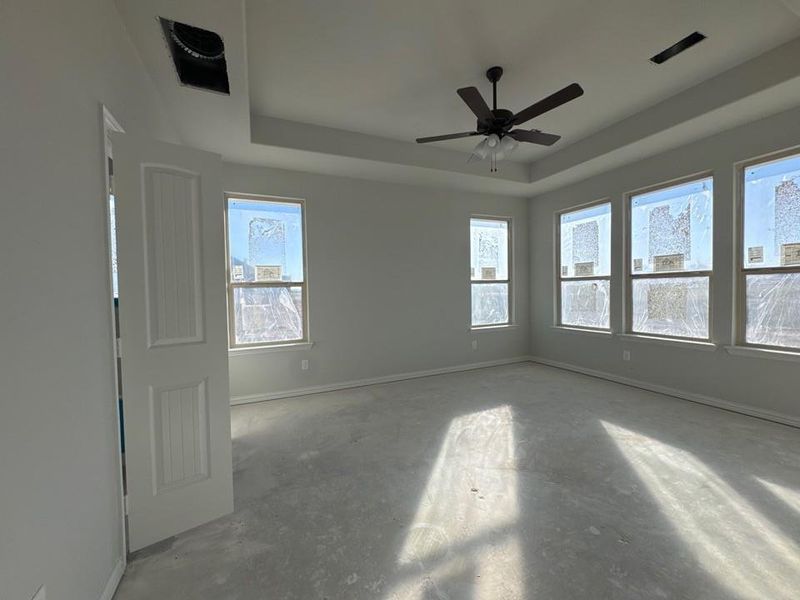 Spare room with a tray ceiling, unfinished concrete floors, and a ceiling fan