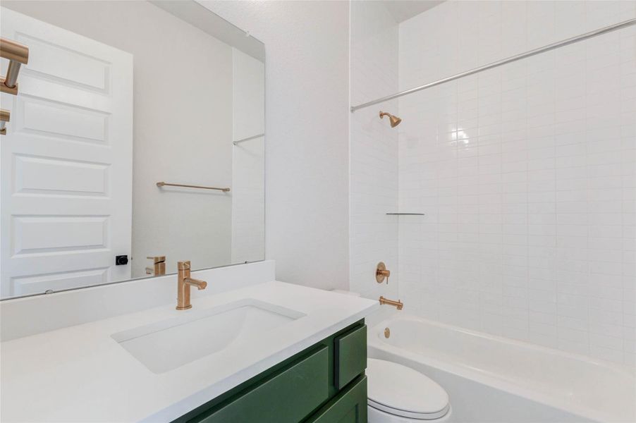 This bathroom features a clean, modern design with a white countertop, green vanity, and elegant gold fixtures. It includes a full bathtub/shower combo with tile to the ceiling.