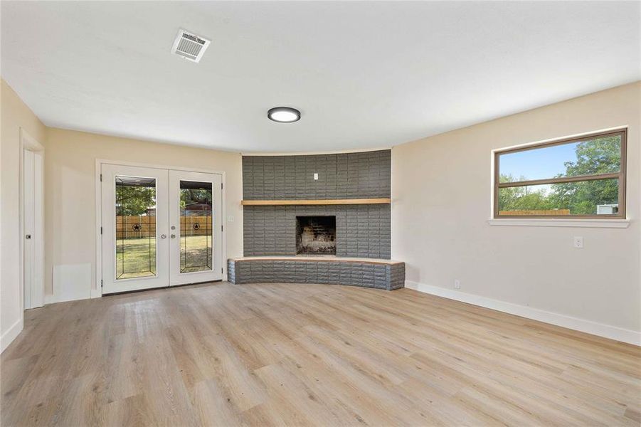 Unfurnished living room with a fireplace, french doors, and light wood finished floors Unfurnished living room with a fireplace, french doors, and light wood finished floors