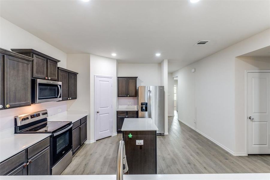 Contemporary kitchen with dark wood cabinetry, white countertops, and stainless steel appliances including an oven range and microwave Contemporary kitchen with dark wood cabinetry, white countertops, and stainless steel appliances including an oven range and microwave