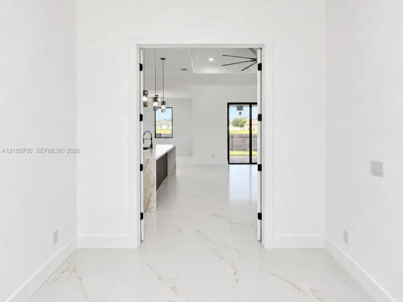 Large-format white tile flooring with veining detail, double-swing interior doors, recessed ceiling lighting, multi-pendant island lighting, and a kitchen island with stone-finish waterfall countertop
