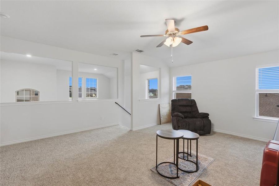 Spacious carpeted room featuring multiple windows, a ceiling fan with light fixture, and recessed lighting