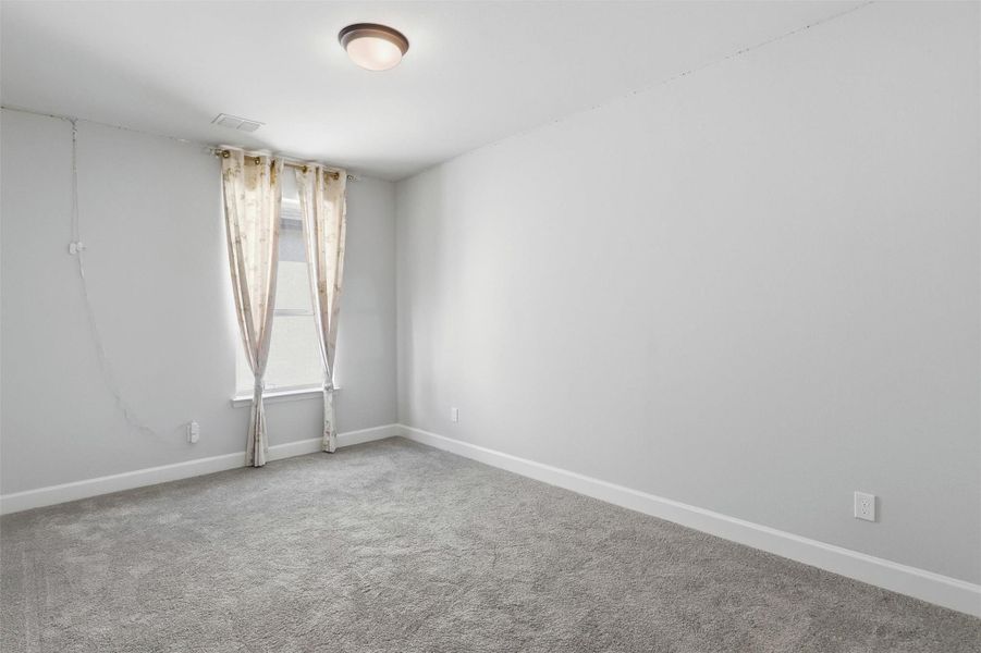 Another spacious secondary bedroom features plush carpeting, neutral finishes, and a large window that fills the room with natural light, creating a comfortable space for family or overnight guests.
