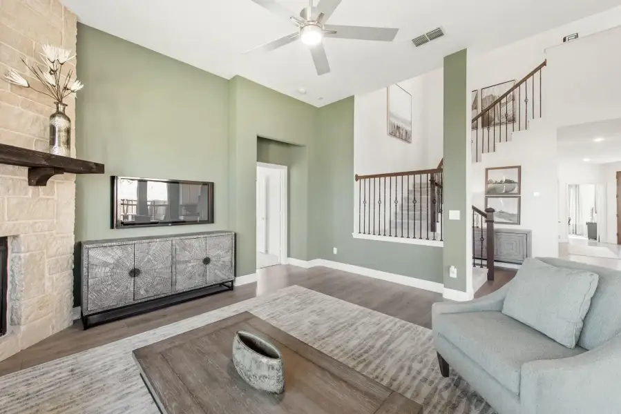 Living room with high ceilings, stone fireplace, ceiling fan, and wood staircase with iron balusters