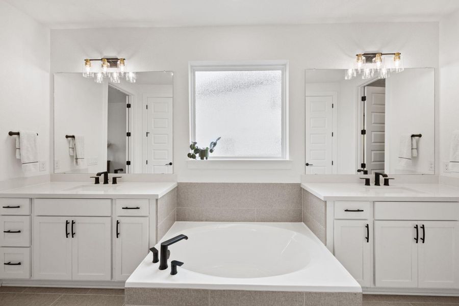 Main level master bathroom with two vanities, a spacious closet, a garden tub, quartz countertops, a shower stall, and recessed lighting.