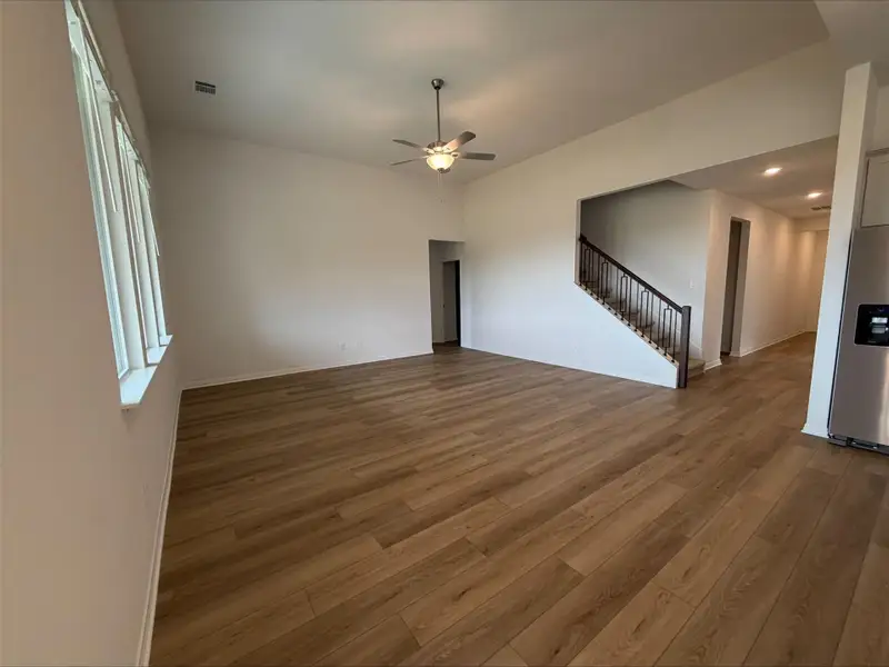 Unfurnished living room featuring dark wood-style flooring, a ceiling fan, and stairway Unfurnished living room featuring dark wood-style flooring, a ceiling fan, and stairway