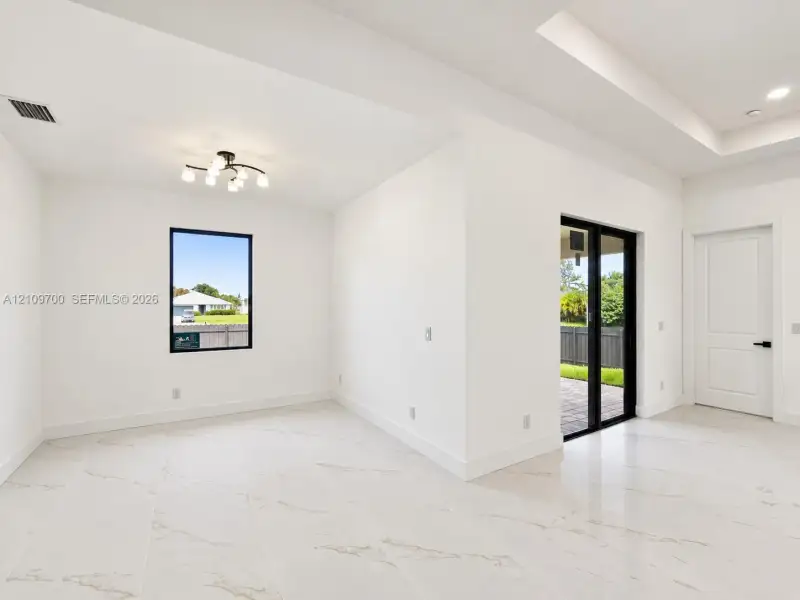 Interior space featuring large-format veined tile flooring, tray ceilings, multi-light modern ceiling fixture, black-framed windows, and sliding glass doors