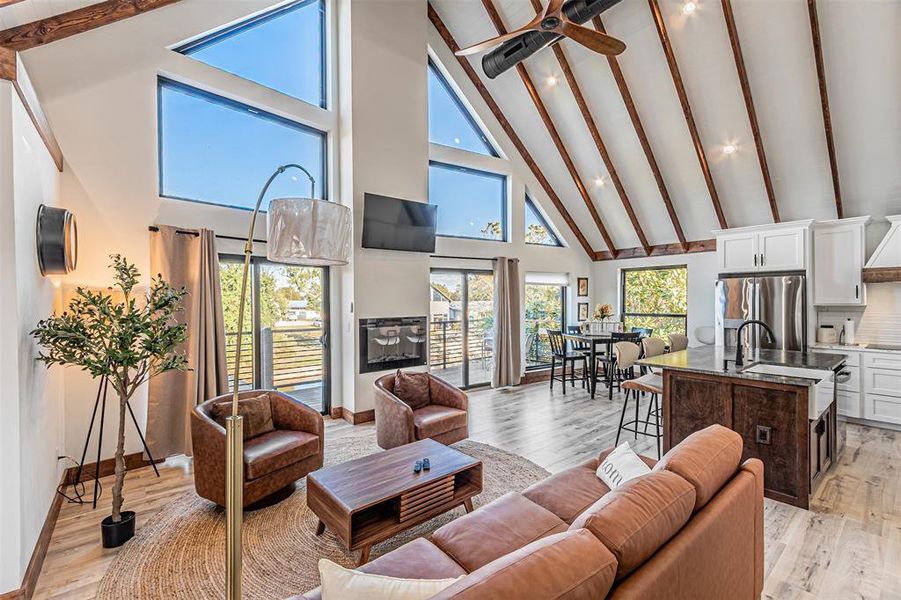 Living room with light wood-style floors, vaulted ceiling, ceiling fan, and a glass covered fireplace