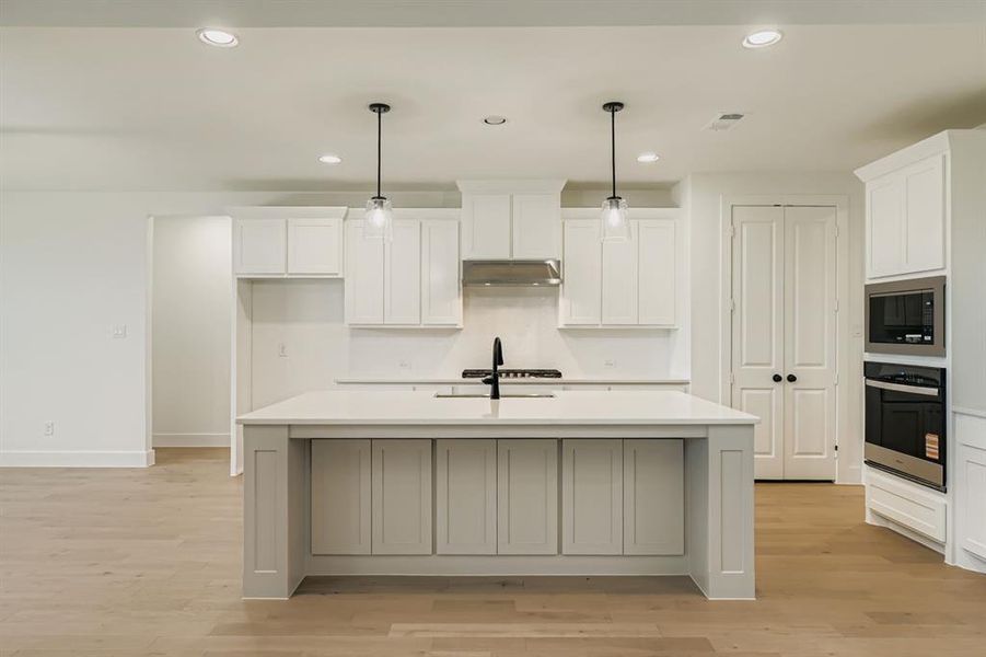 Kitchen with decorative light fixtures, recessed lighting, stainless steel appliances, light wood-type flooring, and a kitchen island with sink Kitchen with decorative light fixtures, recessed lighting, stainless steel appliances, light wood-type flooring, and a kitchen island with sink