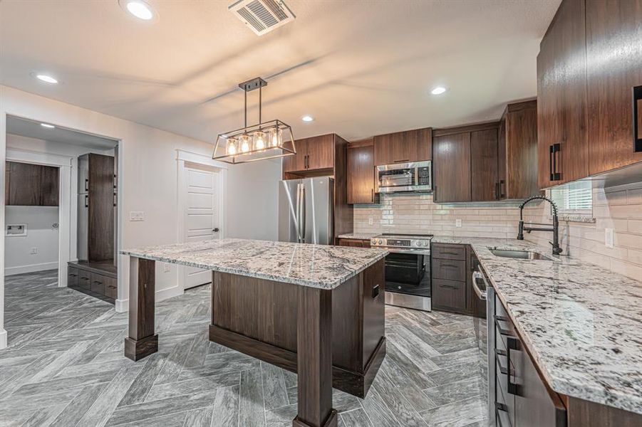 Kitchen with tasteful backsplash, light stone counters, stainless steel appliances, recessed lighting, and dark brown cabinets Kitchen with tasteful backsplash, light stone counters, stainless steel appliances, recessed lighting, and dark brown cabinets