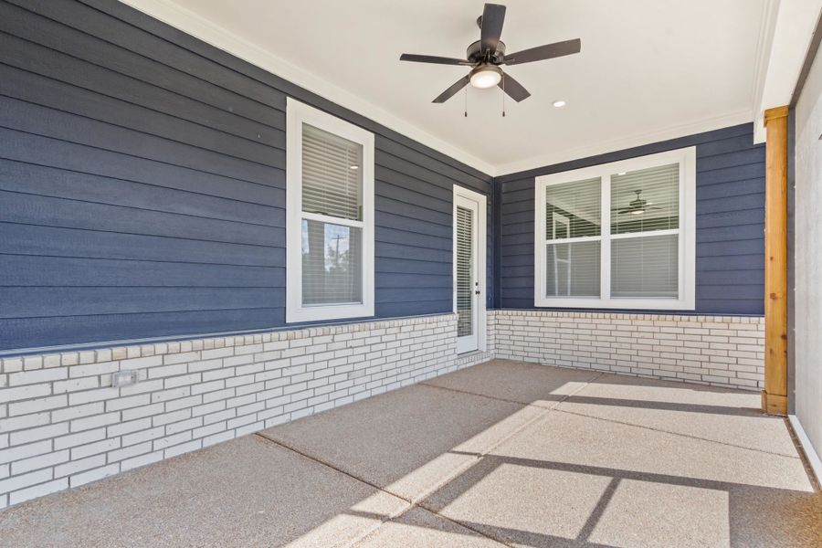 Covered patio featuring a ceiling fan with integrated lighting, exposed aggregate concrete flooring, and an exterior wall finished with blue siding and white brick