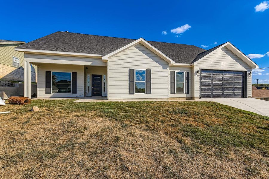 Single story home with a front yard, concrete driveway, an attached garage, covered porch, and roof with shingles