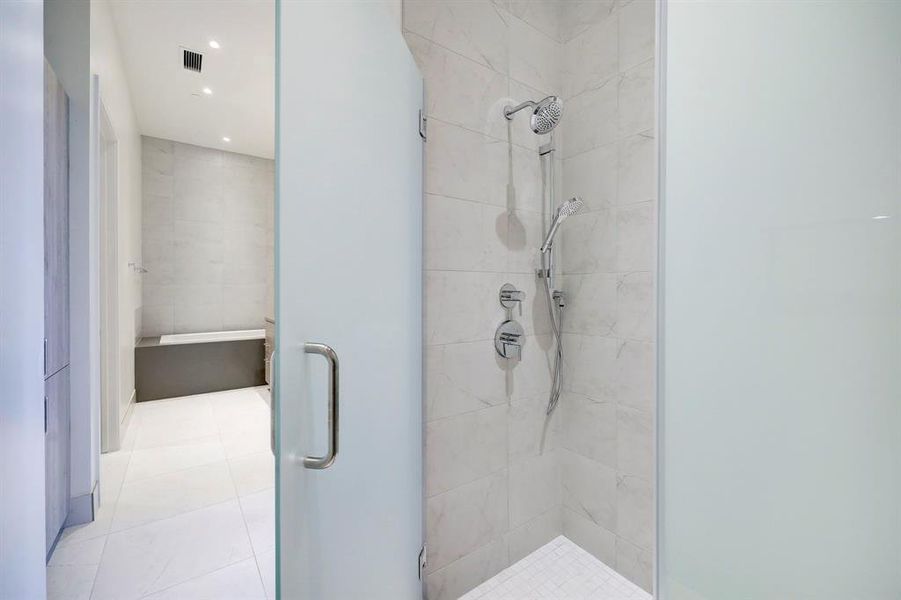 Frosted glass, a rain showerhead and a handheld sprayer ensure calm relaxation in the primary bathroom's inviting walk-in shower.