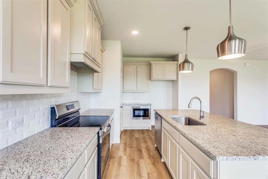 Kitchen featuring an island with sink, pendant lighting, stainless steel appliances, light hardwood / wood-style flooring, and sink