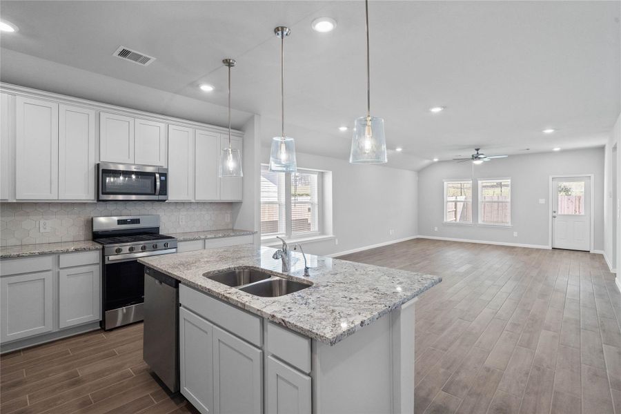 As you step past the entryway, you are immediately welcomed by a bright, open-concept kitchen that serves as the home's focal point. The space feels clean and modern, anchored by a large granite-topped island that seamlessly connects the cooking area to a long, light-filled living space.