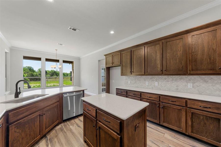 Kitchen featuring stainless steel dishwasher, a sink, ornamental molding, light wood-style flooring, and a chandelier Kitchen featuring stainless steel dishwasher, a sink, ornamental molding, light wood-style flooring, and a chandelier