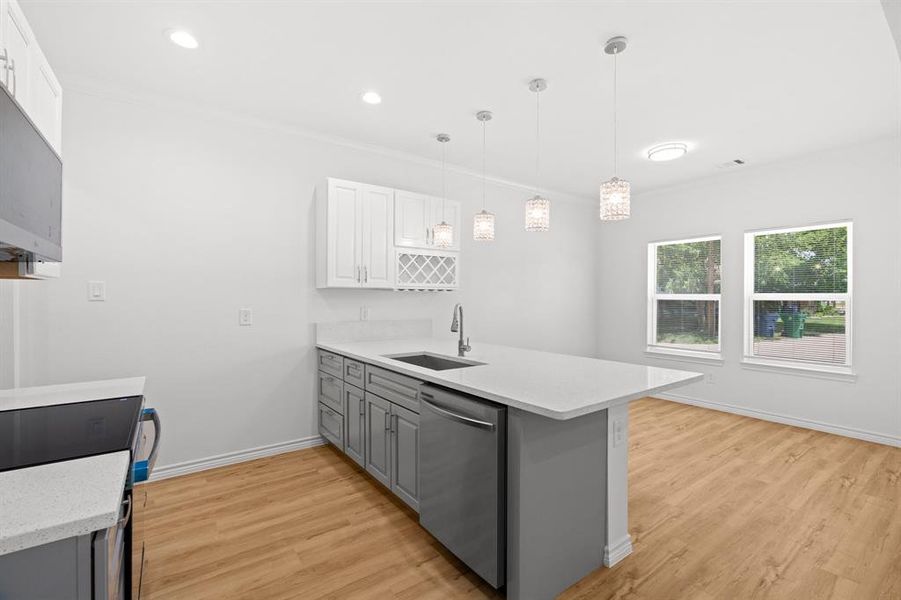 Kitchen with stainless steel dishwasher, gray cabinets, a peninsula, light wood-type flooring, and crown molding Kitchen with stainless steel dishwasher, gray cabinets, a peninsula, light wood-type flooring, and crown molding