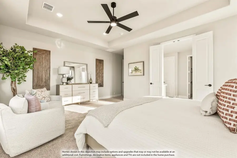 Spacious master bedroom with tray ceiling, ceiling fan, carpet flooring, and double doors leading to ensuite bathroom.